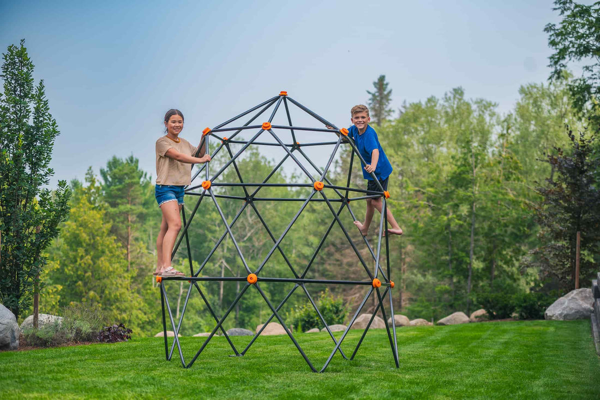 Two kids standing and smiling on a climbing dome.