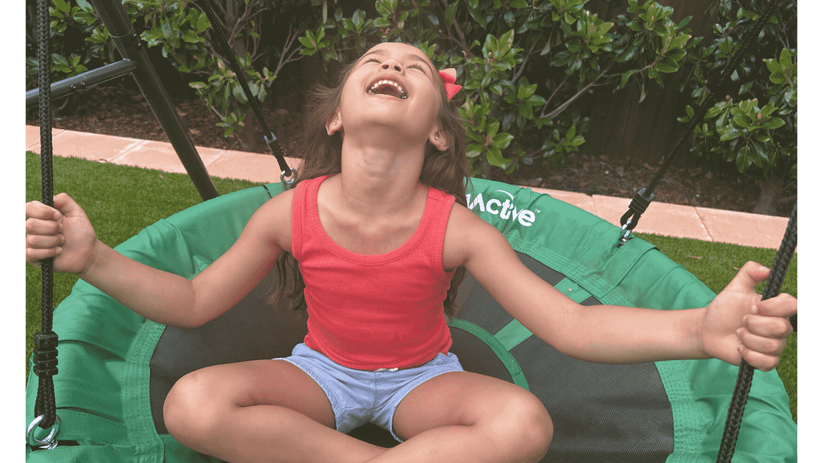 A little girl happily looking up to the sky while on a swing set.